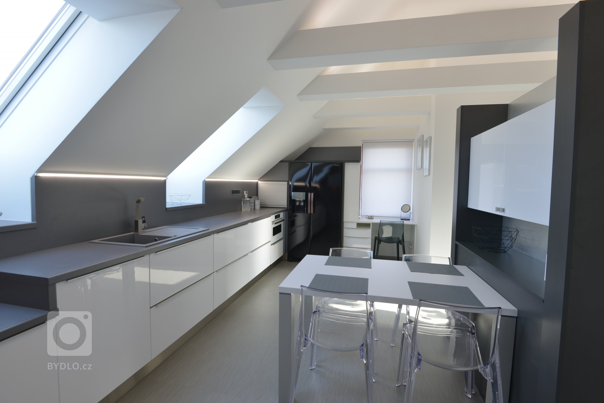 Byt v podkrovním prostoru v domě rodičů. Prostor je rozdělený oboustrannou sestavou, která slouží na televizi a techniku z obývací části a jako jídelna v kuchyňské části. 