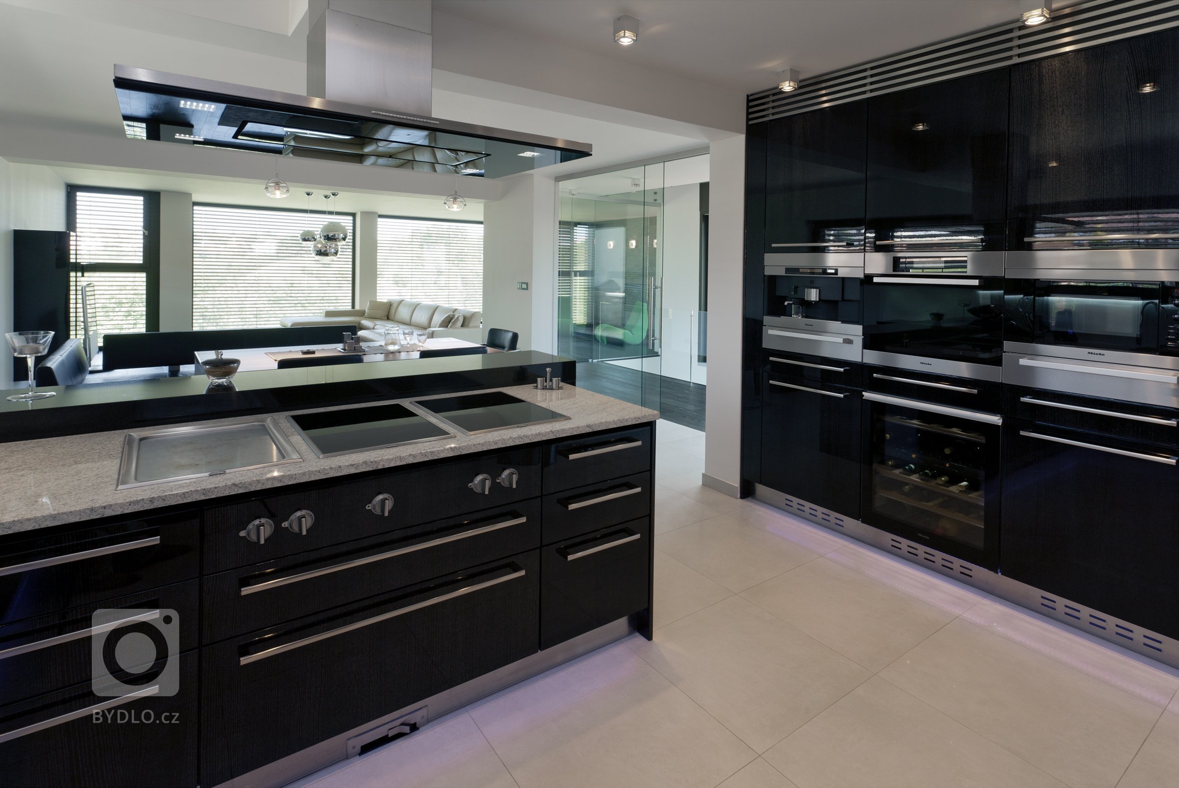 Pohled do kuchyně v černém vysokém lesku se spotřebiči Gaggenau.