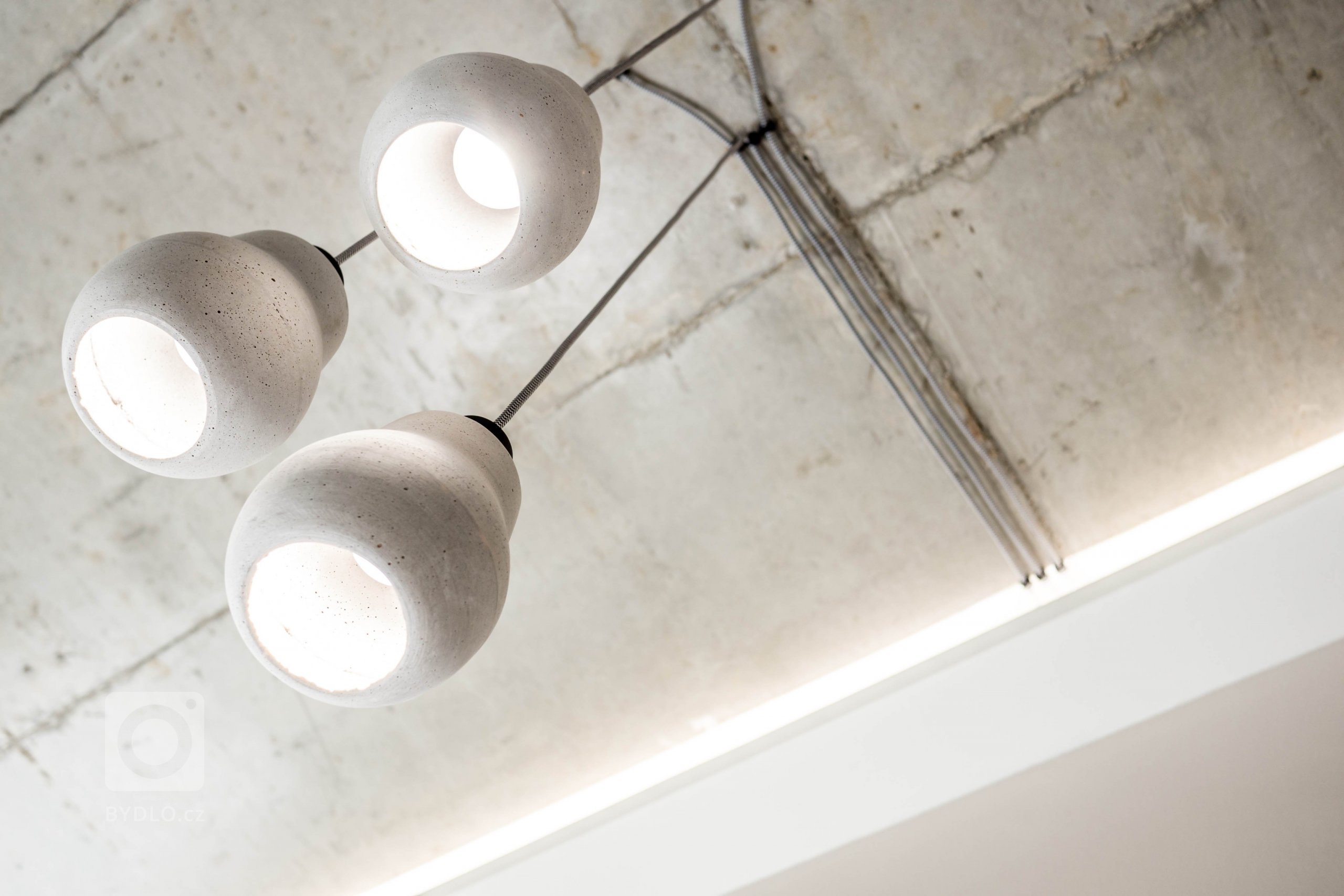 Na betonovém stropě jsou světla vedeny přiznanou kabeláží... design je třeba držet, takže jsme zopakovali materiál stropu i na svítidlech.
